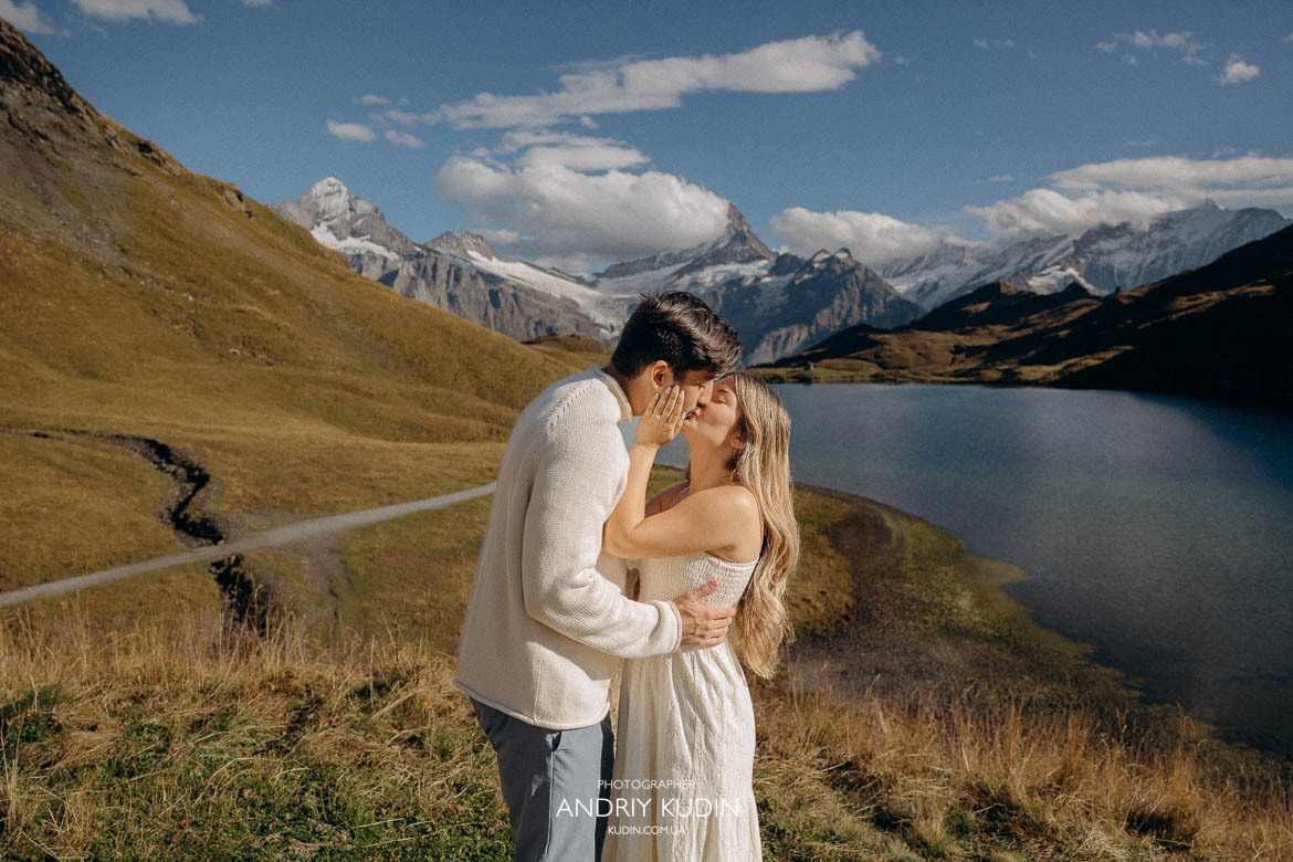A couple sits on a wooden bench by the crystal-clear, turquoise waters of Bachalpsee, lake Bachalp
