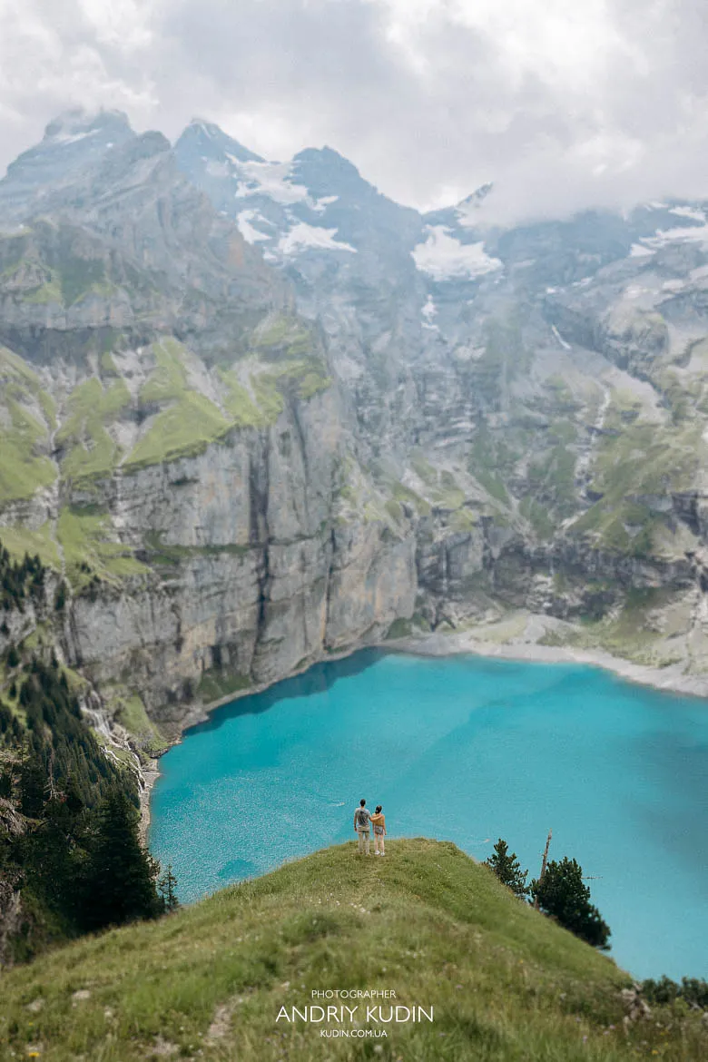 Couple standing on a grassy hill above Oeschinensee during an Oeschinensee proposal, captured by a Switzerland proposal photographer. Couple standing on a grassy hill above Oeschinensee during an Oeschinensee proposal, captured by a Switzerland proposal photographer.