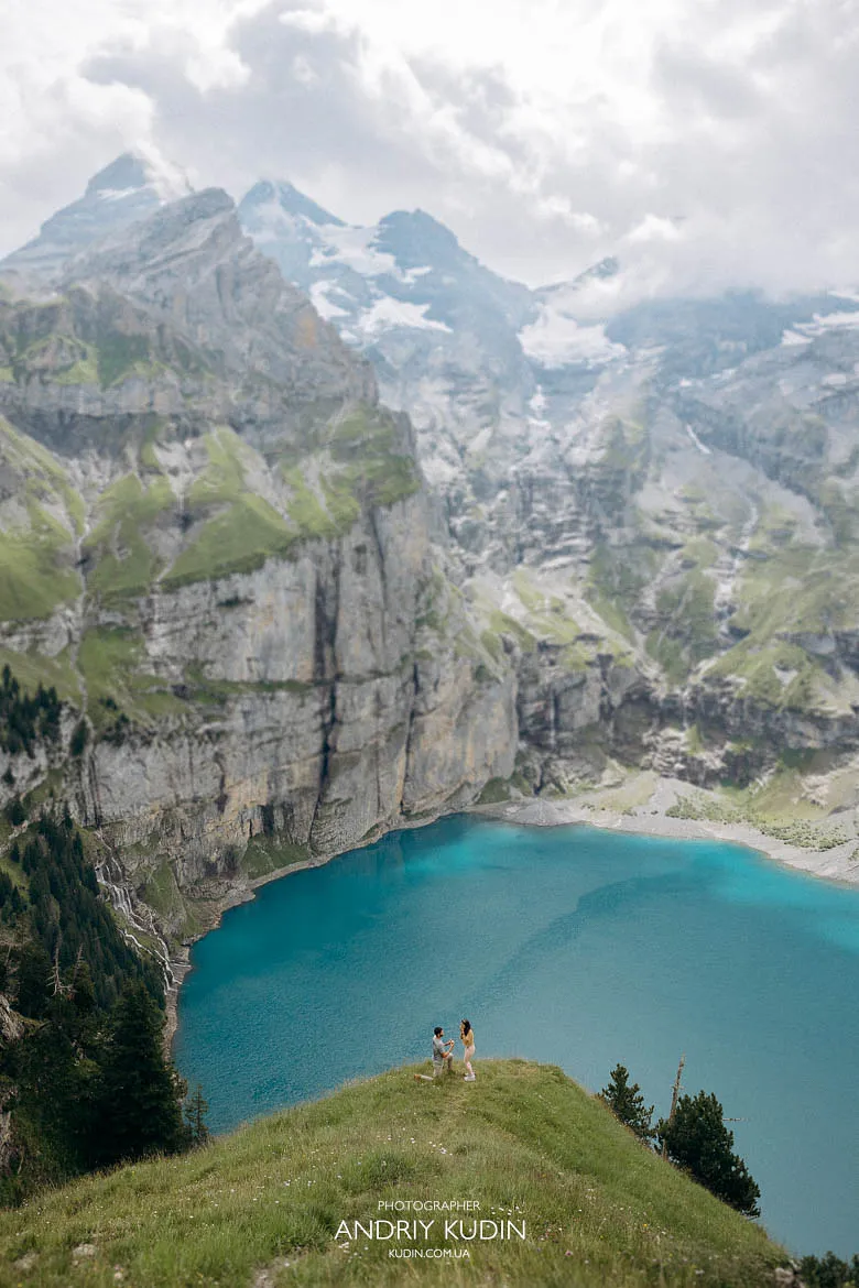 Couple standing on a grassy hill above Oeschinensee during an Oeschinensee proposal, captured by a Switzerland proposal photographer. Couple standing on a grassy hill above Oeschinensee during an Oeschinensee proposal, captured by a Switzerland proposal photographer.