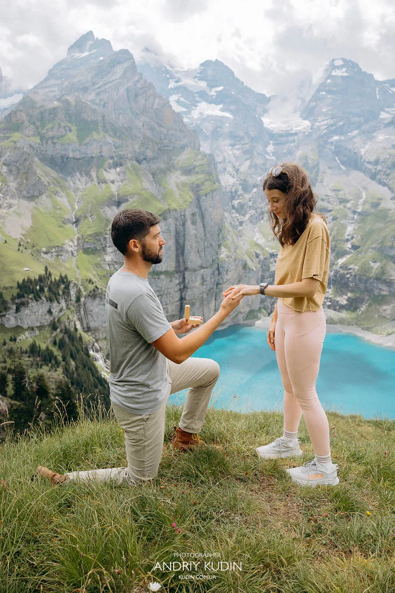 Man kneeling with a ring during an Oeschinensee proposal on a grassy ledge Man kneeling with a ring during an Oeschinensee proposal on a grassy ledge