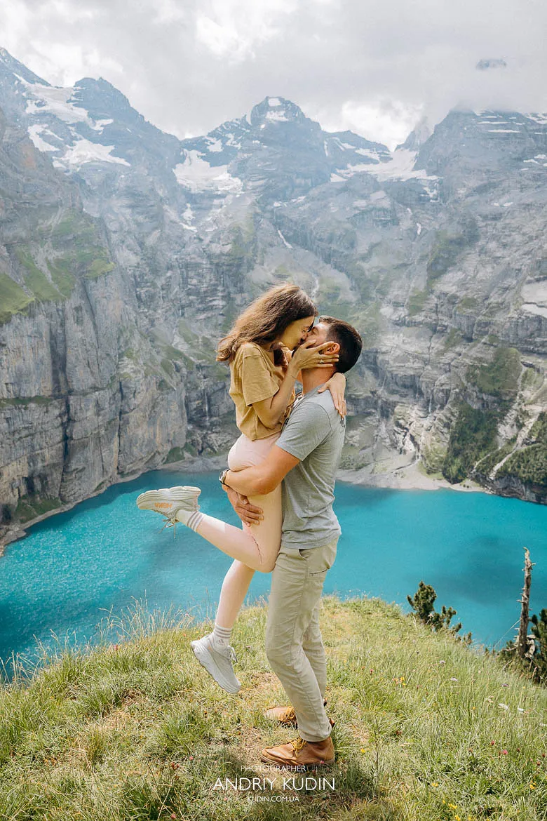 Lake Oeschinen proposal moment with a couple hugging on a grassy viewpoint overlooking the turquoise lake and alpine cliffs Lake Oeschinen proposal moment with a couple hugging on a grassy viewpoint overlooking the turquoise lake and alpine cliffs