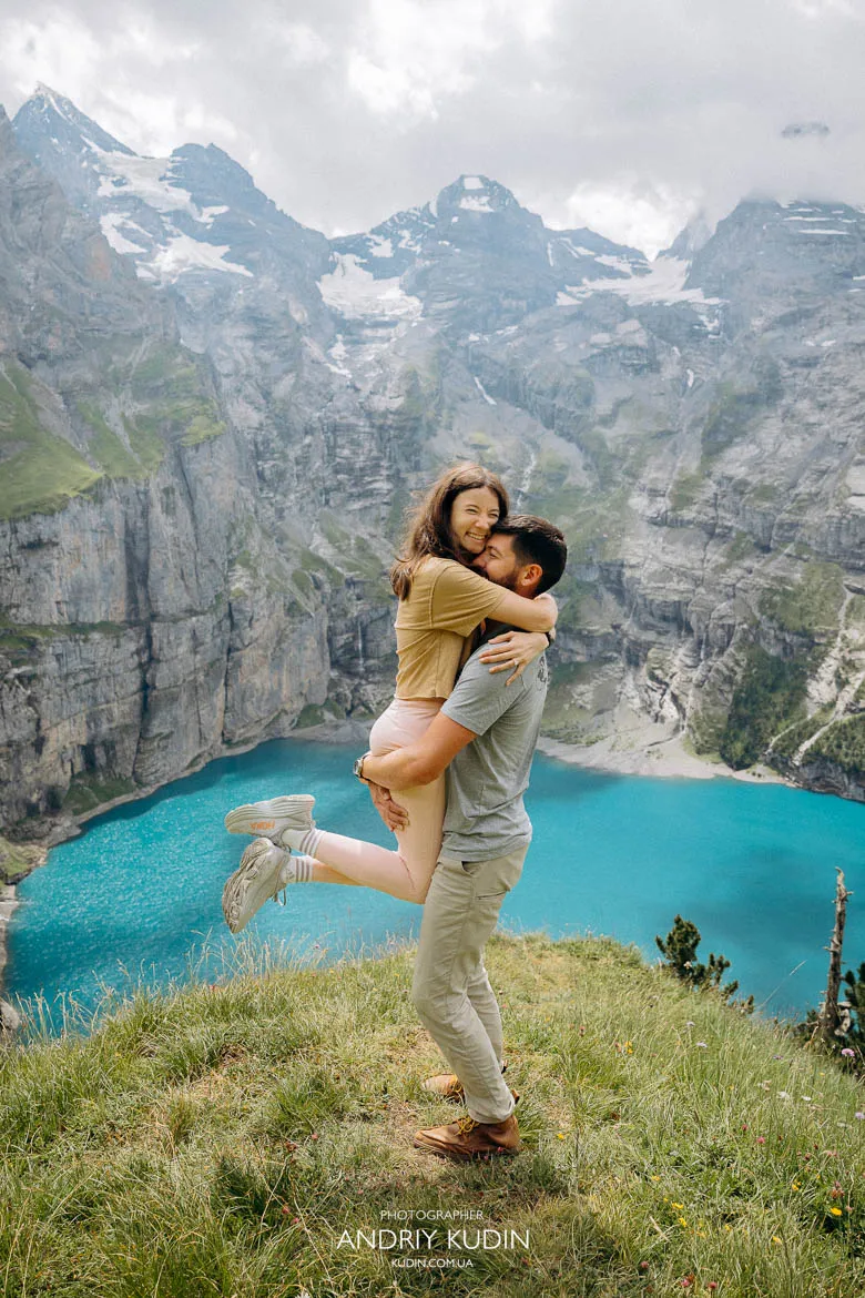 Couple embracing on a grassy cliff above Lake Oeschinen during a Lake Oeschinen proposal Couple embracing on a grassy cliff above Lake Oeschinen during a Lake Oeschinen proposal