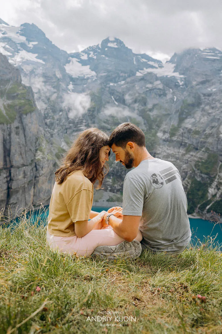 Couple sitting close together on a grassy cliff above Lake Oeschinen Couple sitting close together on a grassy cliff above Lake Oeschinen