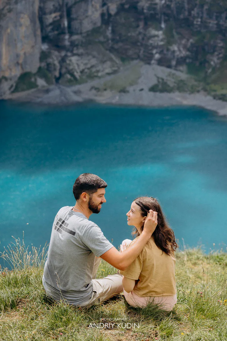 Marriage proposal photography at Lake Oeschinen showing a couple seated on a grassy viewpoint with turquoise water and rocky cliffs in Switzerland. Marriage proposal photography at Lake Oeschinen showing a couple seated on a grassy viewpoint with turquoise water and rocky cliffs in Switzerland.
