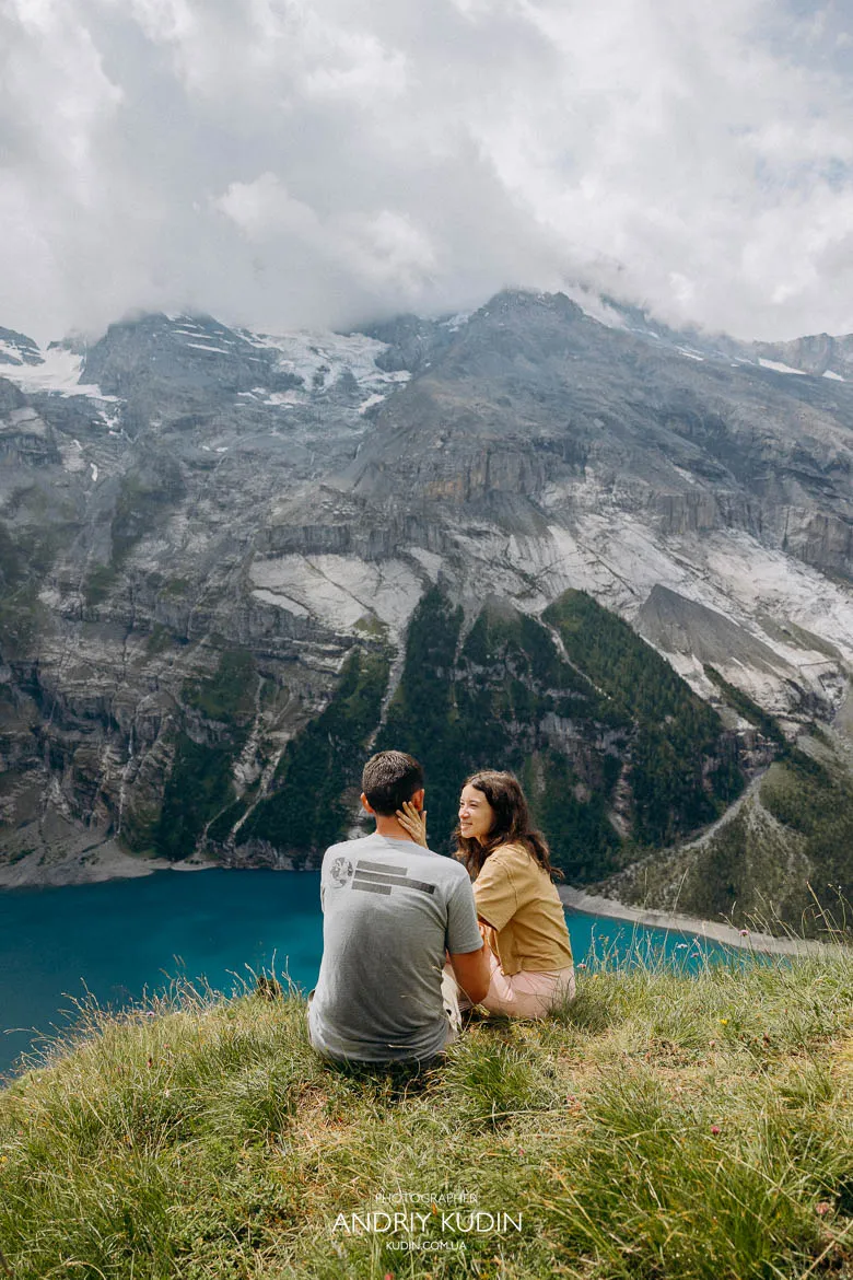 Couple sitting on a grassy cliff above Lake Oeschinen during a Lake Oeschinen proposal Couple sitting on a grassy cliff above Lake Oeschinen during a Lake Oeschinen proposal