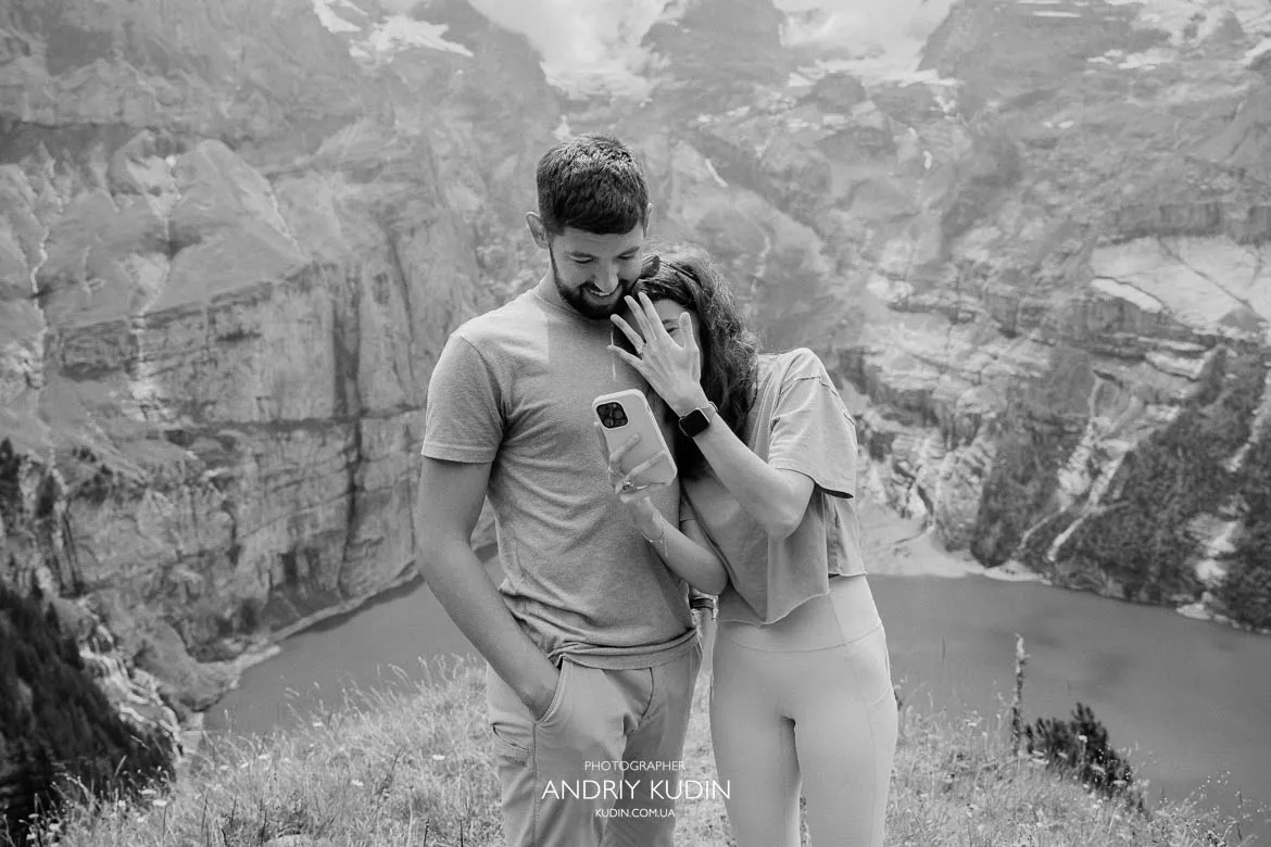couple standing close on a grassy ledge overlooking the lake and rocky mountains.