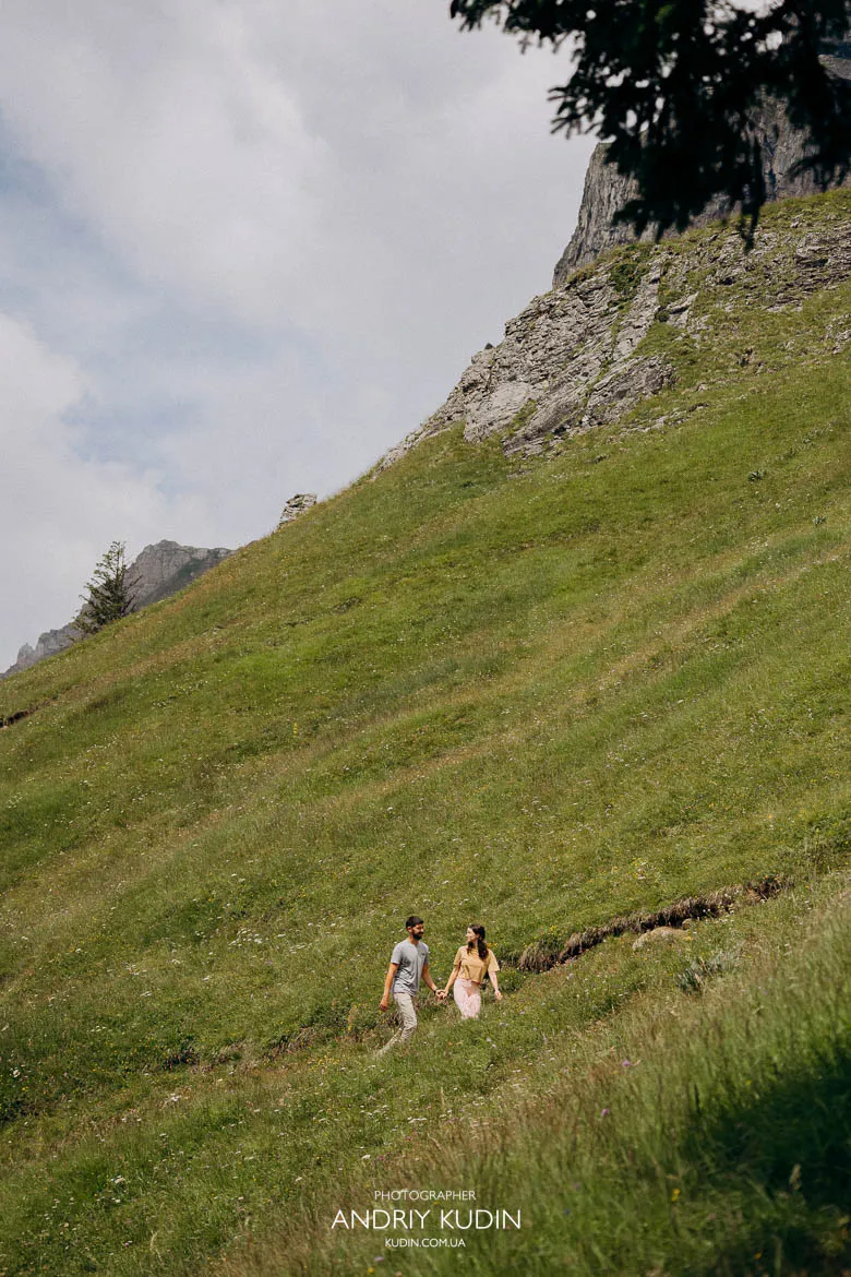 Couple walking hand in hand on a grassy hillside above Lake Oeschinen