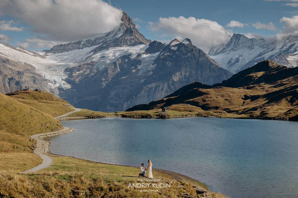 Man kneeling with engagement ring by an alpine lake in Grindelwald.