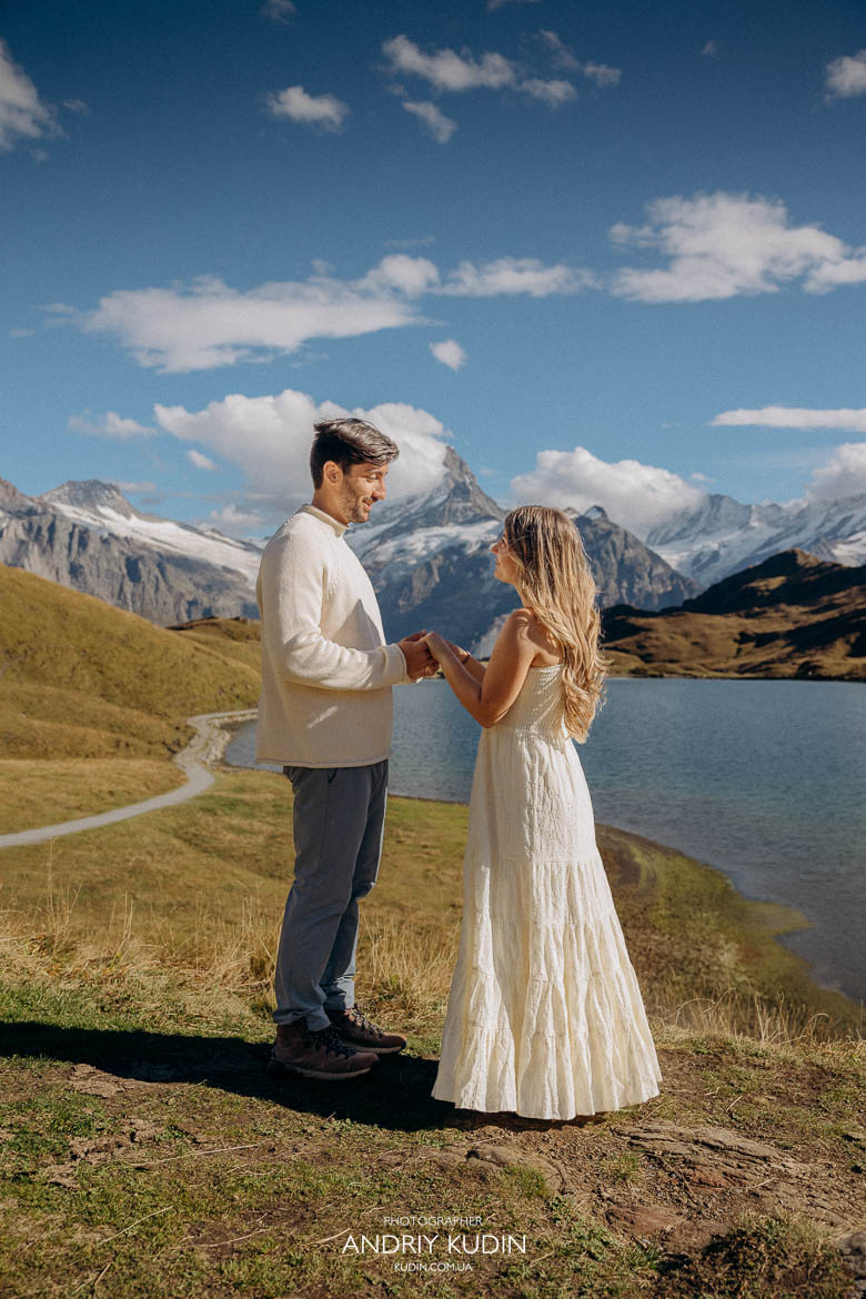Couple holding hands by turquoise alpine lake during engagement.