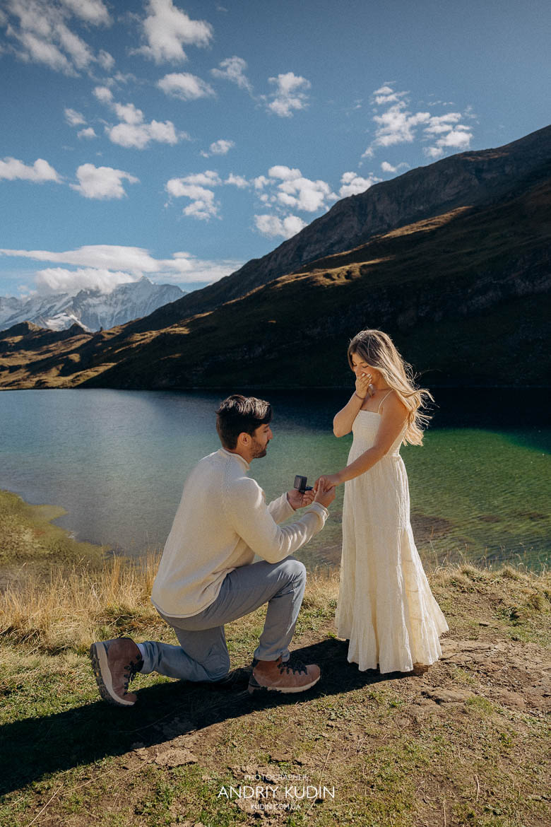 Man kneeling with engagement ring by an alpine lake in Grindelwald.