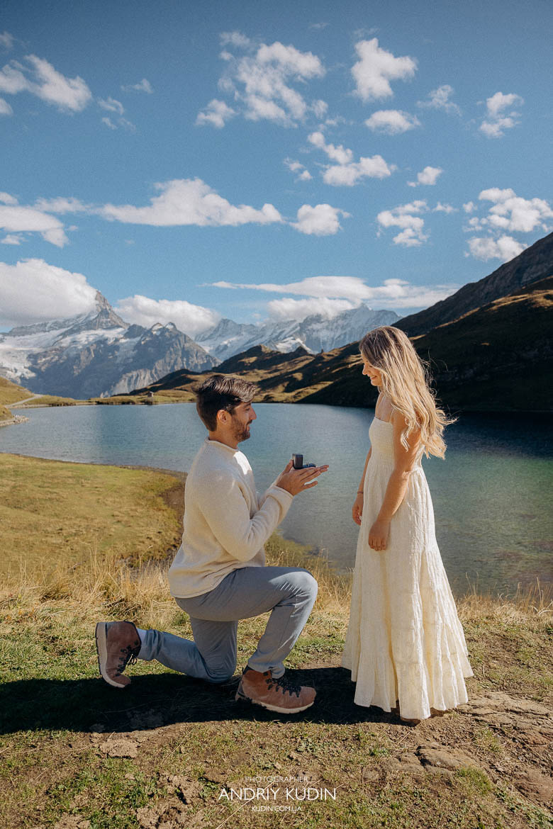 Man kneeling with engagement ring by an alpine lake in Grindelwald.