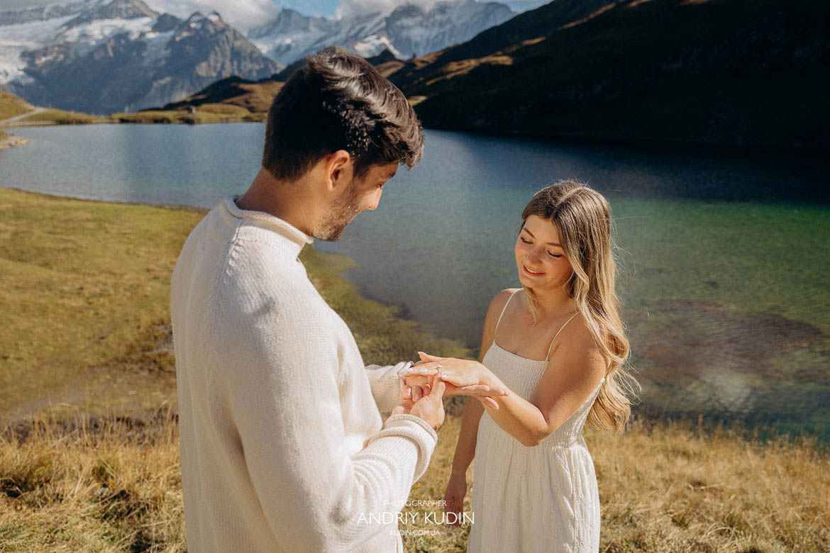 Man proposing on a mountain trail with alpine view behind.