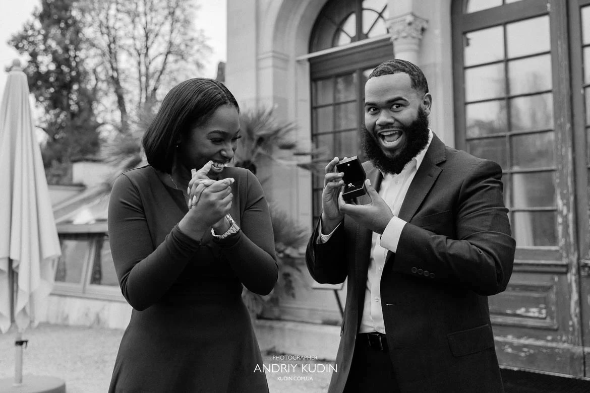Black and white portrait of excited groom-to-be holding open ring box with emotional bride-to-be in Zurich