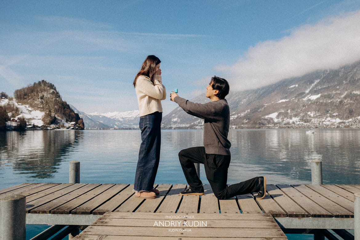 Groom proposing on wooden pier in Iseltwald Switzerland during a marriage proposal by Lake Brienz