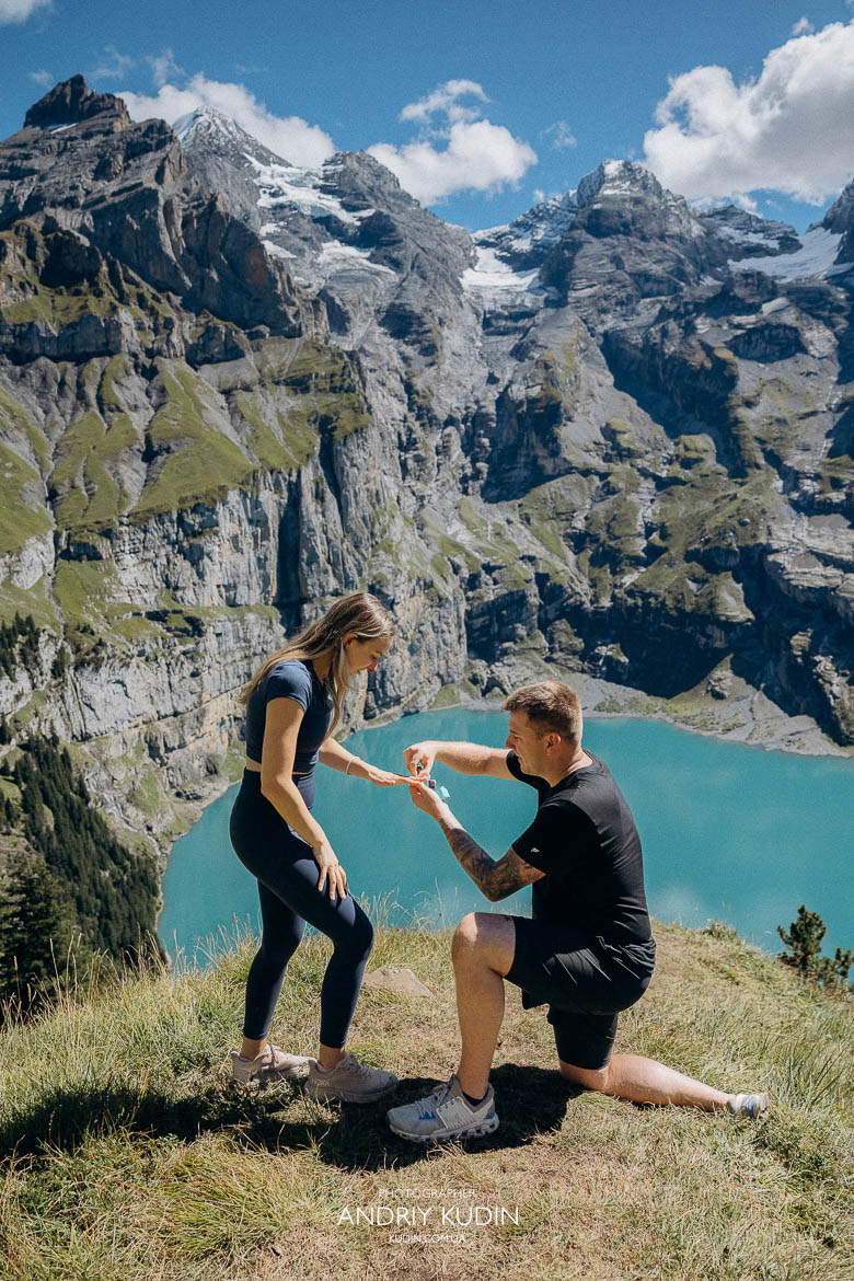 Man on one knee proposing above Lake Oeschinensee Emotional reaction during surprise proposal at Lake Oeschinen