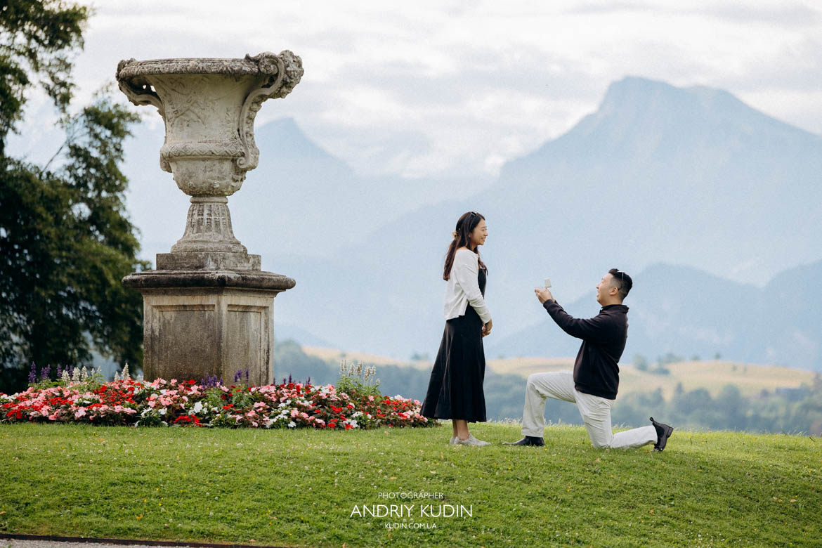 Man kneeling on one knee during a surprise marriage proposal in a quiet park above Lucerne.
