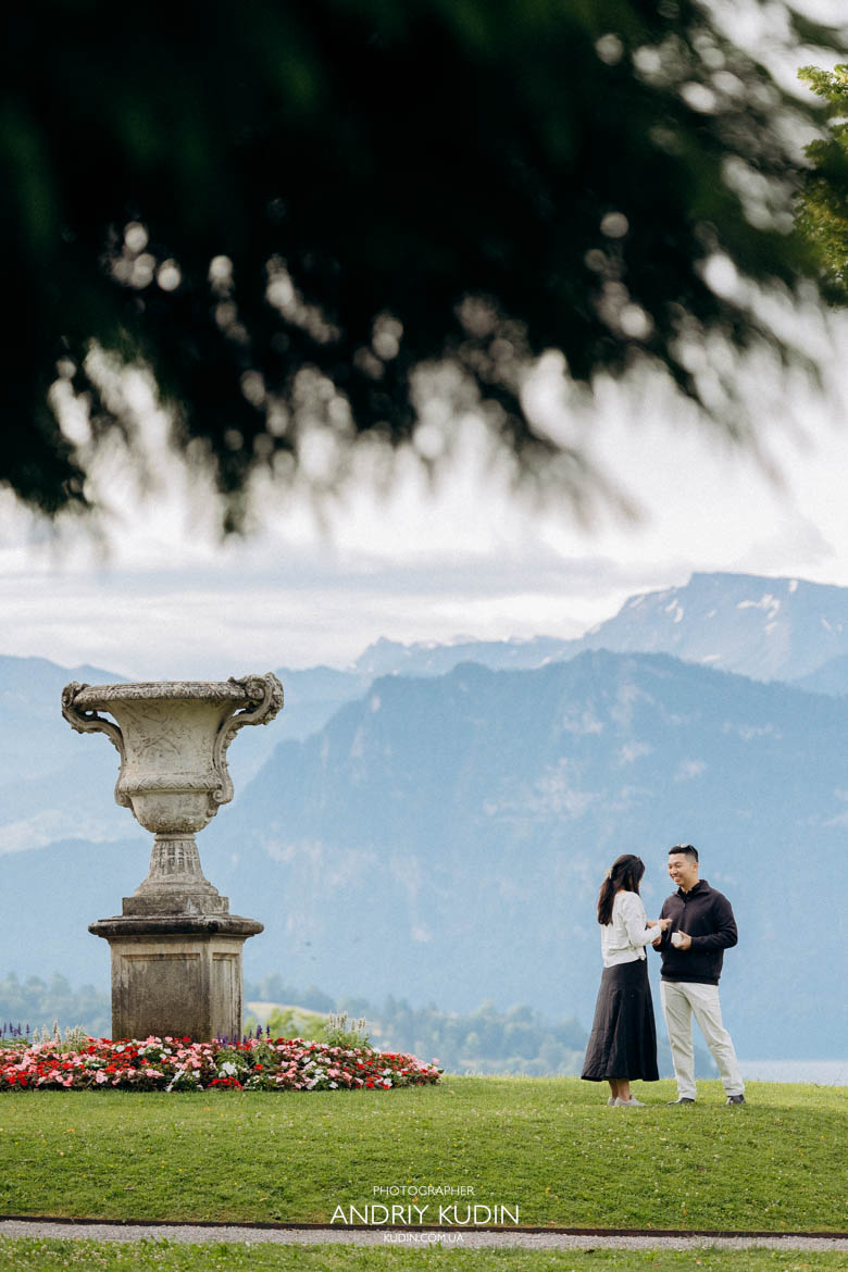 Epic proposal shot featuring the dramatic peak of Mount Pilatus behind the kneeling couple. Romantic morning proposal with no tourists around in a scenic park above Lucerne city.