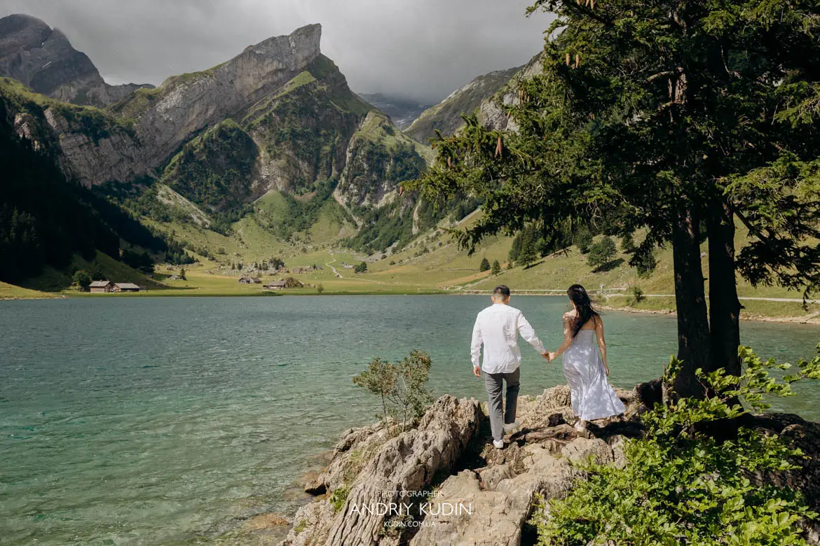 Panoramic view of engaged couple walking hand in hand by turquoise mountain lake in Appenzell Switzerland