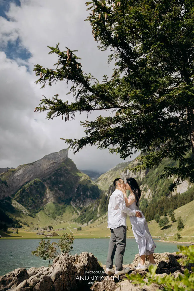 Romantic couple kissing under pine branches with alpine mountain and Seealpsee lake in background
