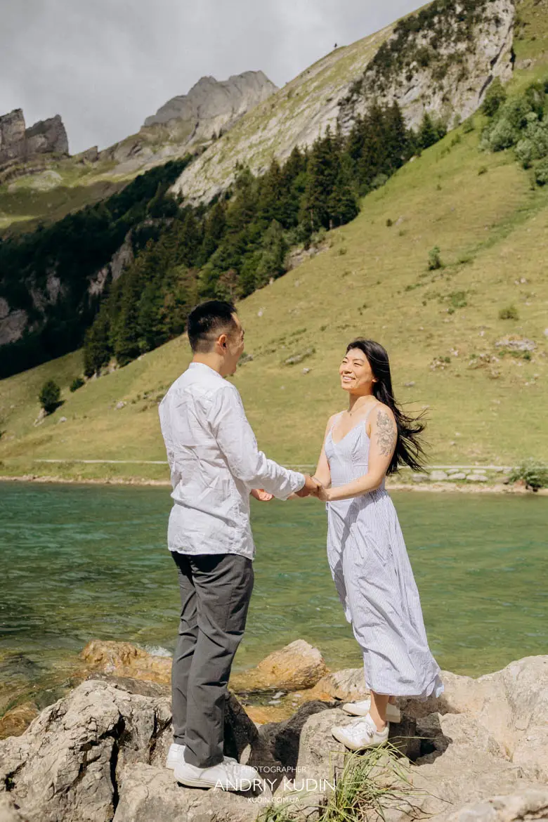 Happy newly engaged couple laughing and holding hands at Seealpsee lake shore in Swiss Alps