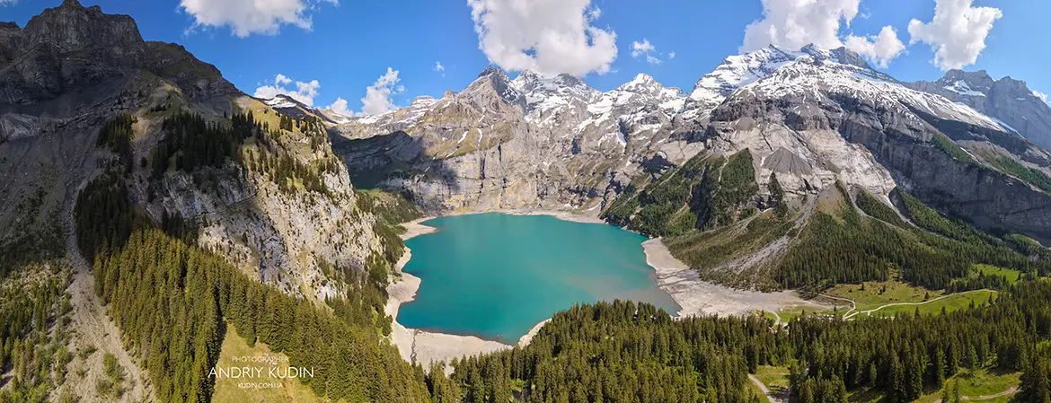 Aerial panorama of turquoise Lake Oeschinensee surrounded by dramatic mountain cliffs