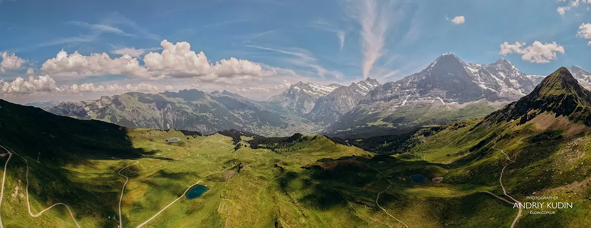 Aerial shot of green alpine ridge with snow covered mountain peaks background