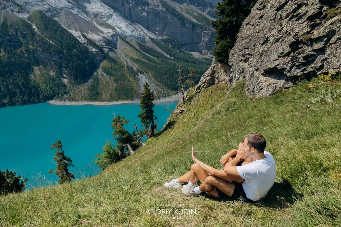 Holden and Misha embracing with blue alpine lake background after secret proposal