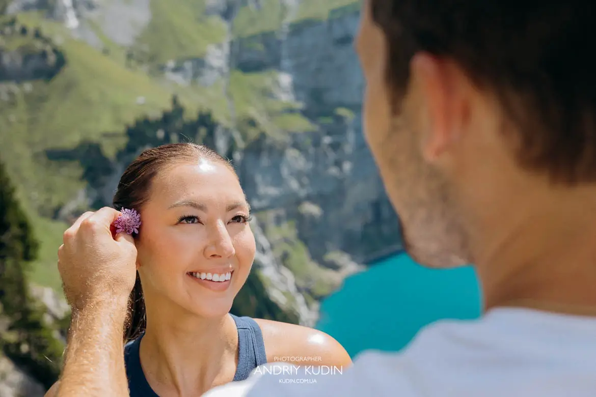 Surprise engagement proposal moment on the mountain cliff above Lake Oeschinensee