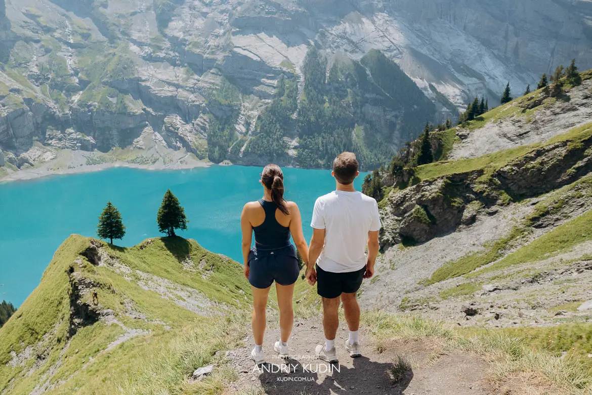 Panoramic view of two iconic pine trees on the cliff edge overlooking turquoise Lake Oeschinensee