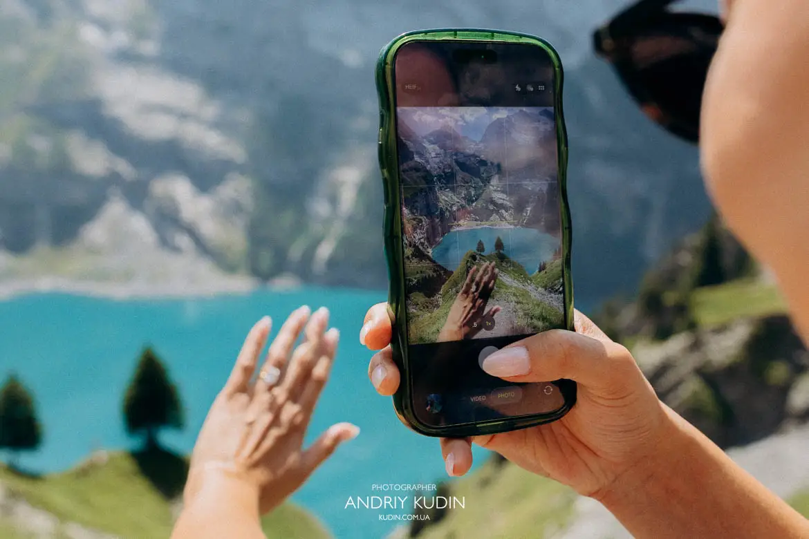 Taking a smartphone picture of engagement ring with iconic Oeschinensee two pine trees backdrop