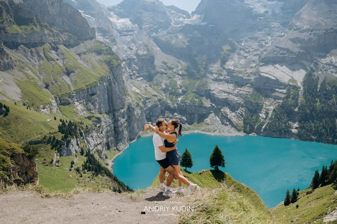 Newly engaged couple embracing with blue alpine lake background after secret proposal
