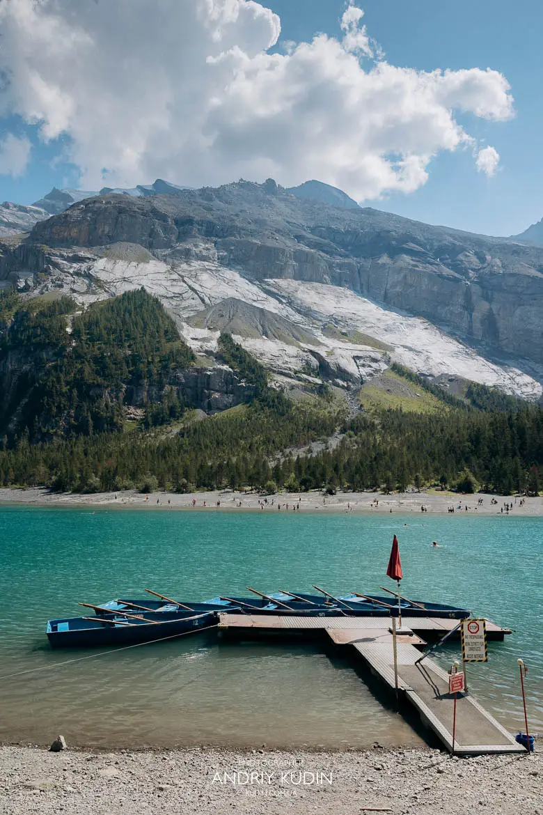 Vertical view of wooden rowboat rental dock on turquoise shore of Oeschinensee with towering cliffs
