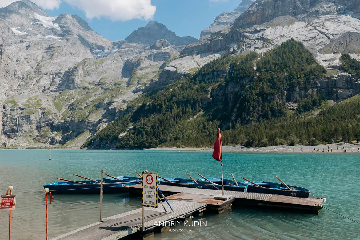 Blue wooden rowboats docked at Lake Oeschinen pier with massive Swiss Alps mountain peaks background