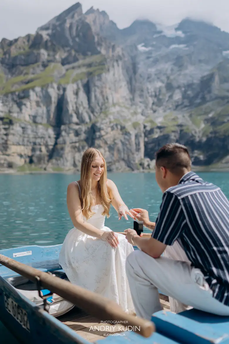 Man putting engagement ring on fiancee hand during surprise rowboat proposal at Lake Oeschinen Swiss Alps