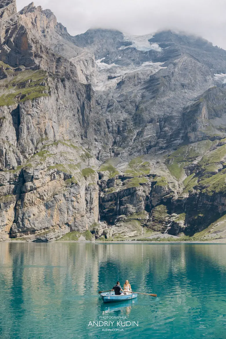 Vertical photo of engaged couple in a blue wooden rowboat on Lake Oeschinen captured by switzerland proposal photographer
