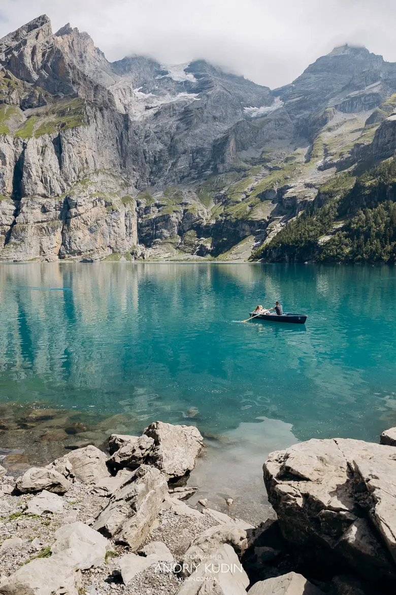 Scenic view of couple rowing a boat on turquoise Lake Oeschinen surrounded by massive Swiss Alps cliffs