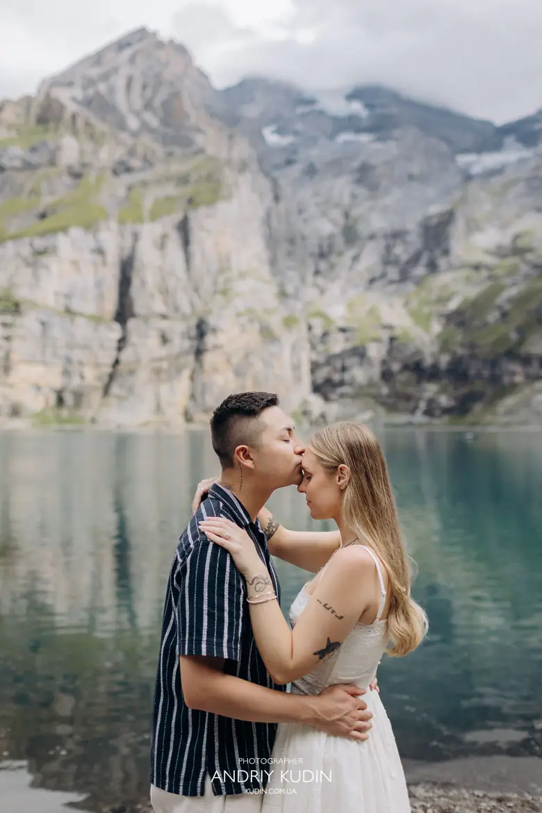 Groom kissing bride on forehead by Lake Oeschinen shore captured by switzerland proposal photographer