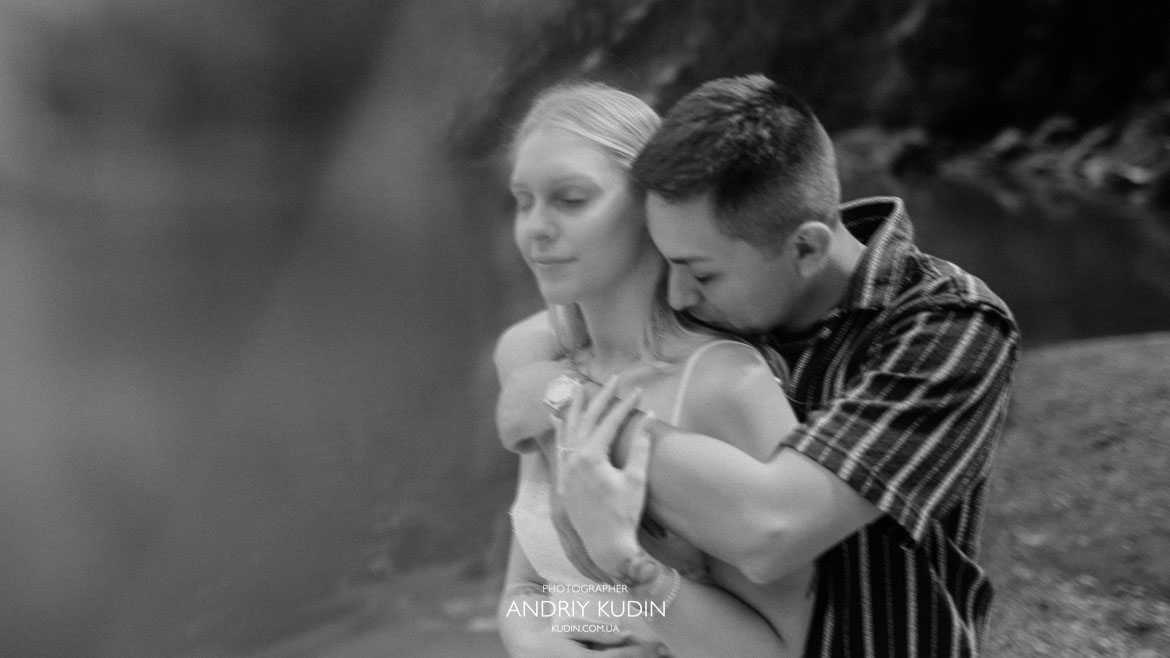 Black and white intimate portrait of groom embracing bride from behind near Lake Oeschinen by switzerland proposal photographer