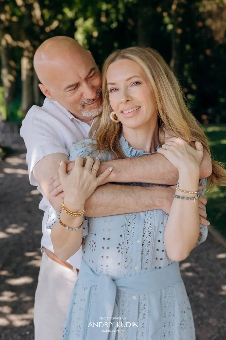 Man embracing smiling wife in light blue dress during couple session in Swiss park