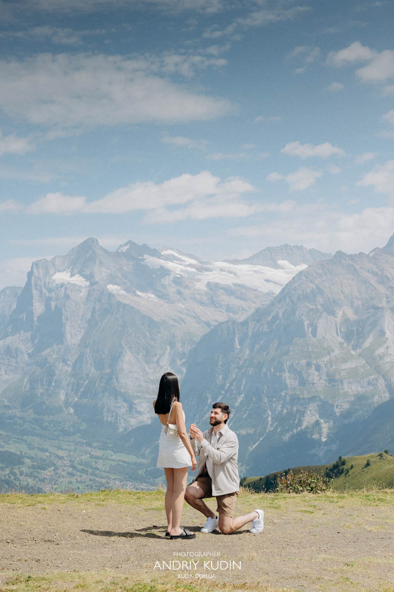 Surprise proposal on Mannlichen with ring Surprise proposal on Mannlichen man on one knee with ring in front of Eiger Mönch and Jungfrau mountains by switzerland proposal photographer