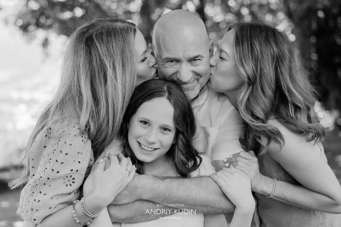 Emotional black and white photo of happy father surrounded by wife and daughters during family session