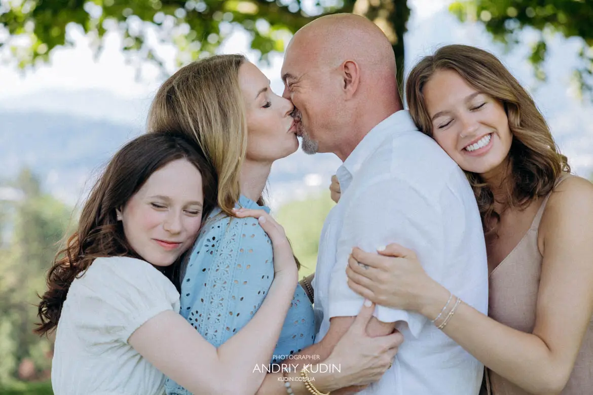Parents kissing while two daughters embrace them during family photoshoot in Switzerland