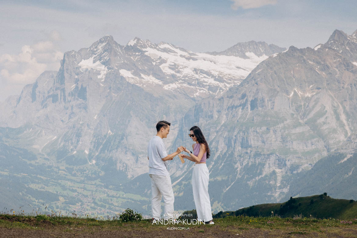 Groom putting engagement ring on brides finger during surprise proposal in Bernese Alps Switzerland