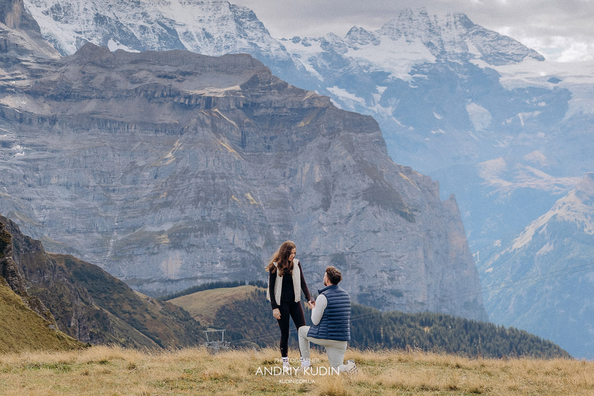 Man kneeling to propose to his girlfriend on Mannlichen ridge with iconic Swiss Alps mountain backdrop