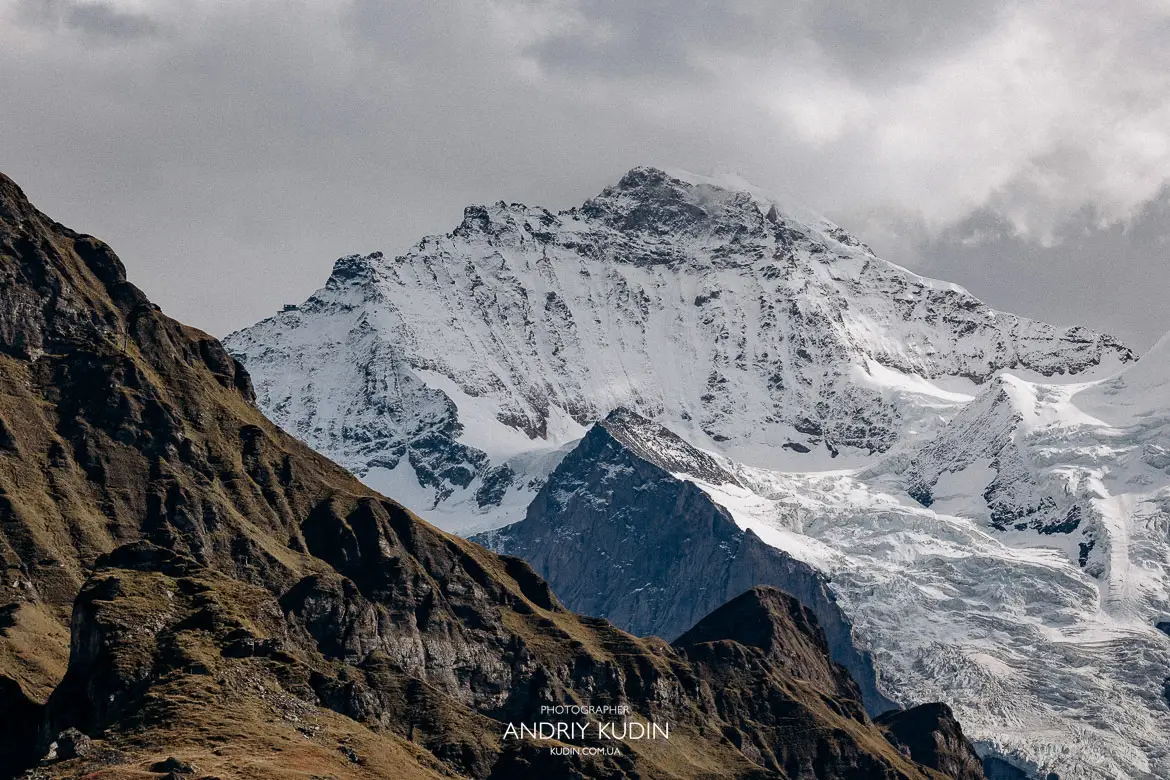 Scenic view of Swiss flag waving on high mountain ridge with dramatic Alps peak and clouds background in Mannlichen Switzerland