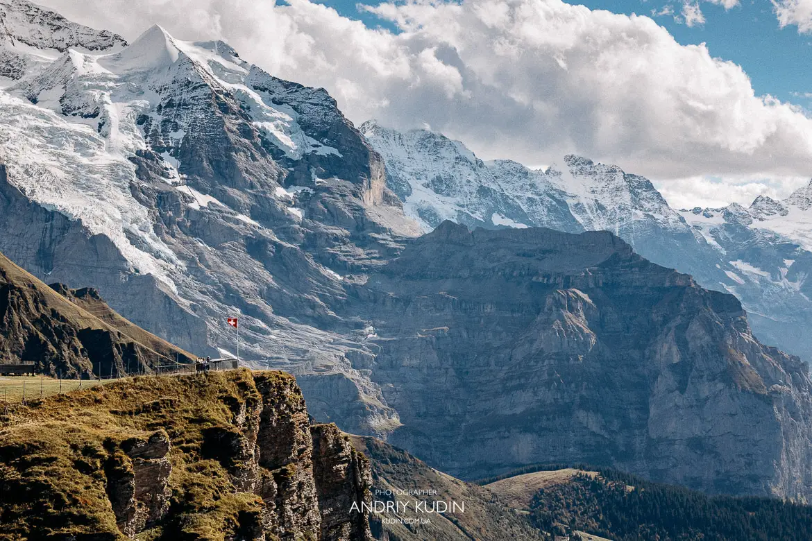 Dramatic Swiss Alps landscape featuring mountain cliff with waving flag taken during engagement photoshoot in Bernese Oberland