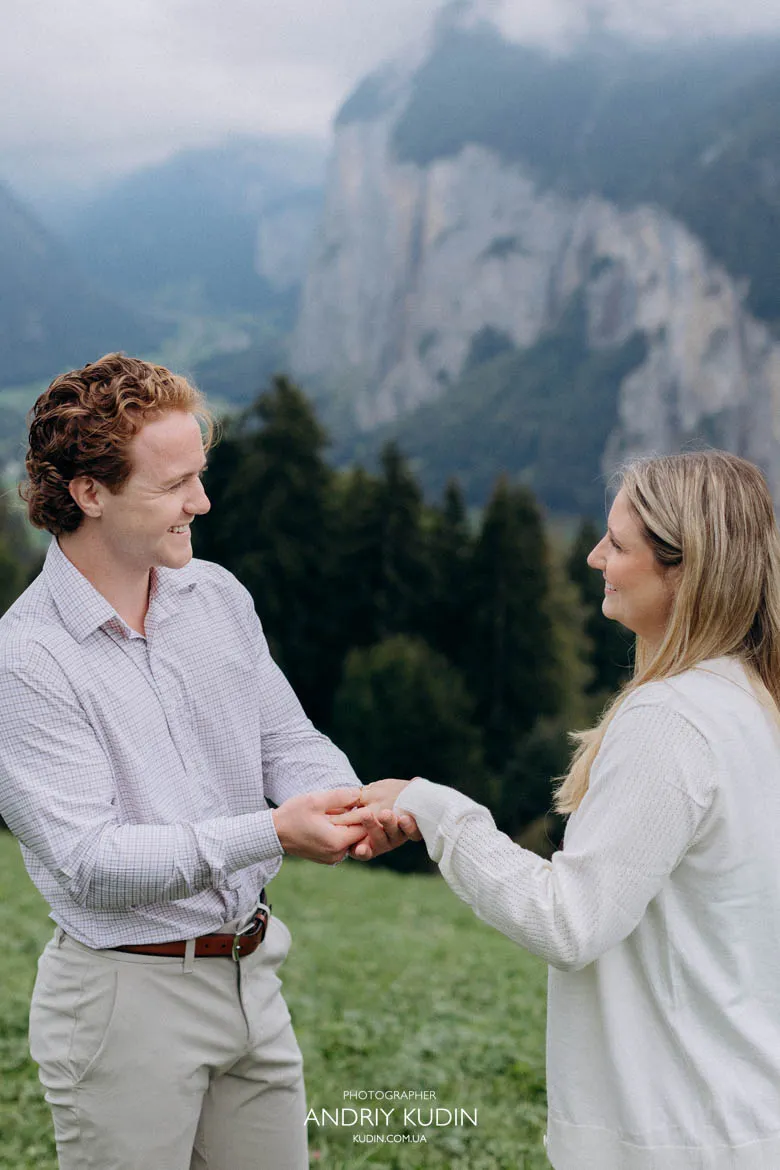 Couple posing in green alpine meadow with dramatic waterfalls and steep cliffs in Lauterbrunnen.