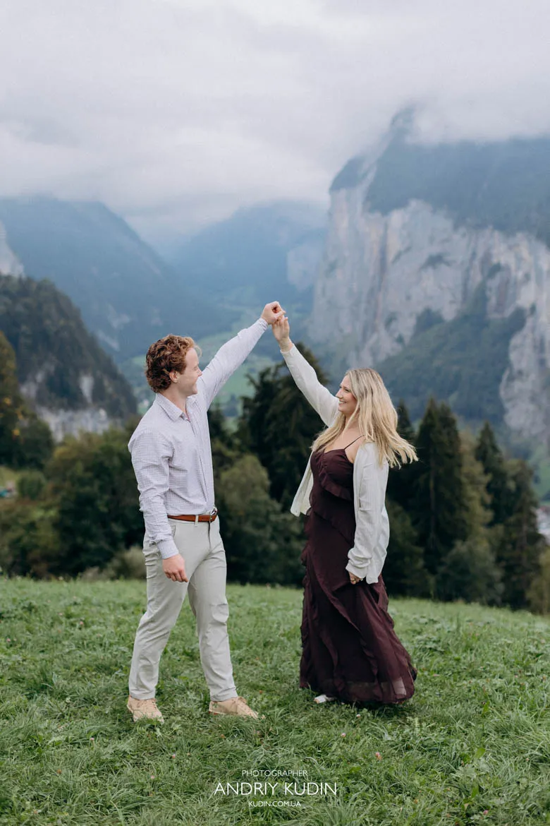 Engaged couple dancing together in green meadow overlooking Lauterbrunnen Valley. Photo by switzerland proposal photographer.