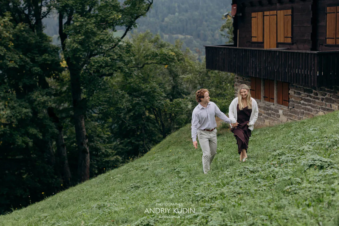 Engaged couple walking down grassy slope near chalet in Lauterbrunnen. Photo by switzerland proposal photographer.