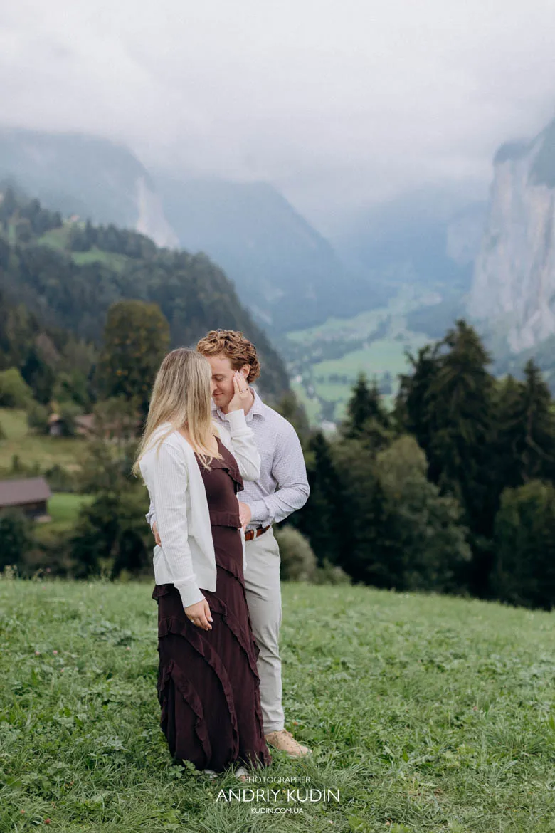 Engaged couple standing in alpine field overlooking Lauterbrunnen Valley. Photo by switzerland proposal photographer.